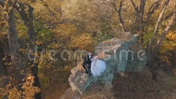 新婚夫妇可爱的新郎和新娘坐在森林里一座被摧毁的建筑物的遗骸上家庭幸福男子和妇女视频的预览图