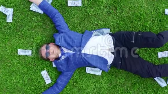 年轻的商人学生或上班族躺在一片长满了钱的绿草草地上视频的预览图