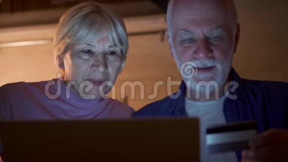 一对老夫妇晚上在家厨房退休家庭用笔记本电脑上网购物视频的预览图