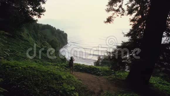 旅游女孩在智能手机上拍照站在悬崖山上日落时山林中的海浪视频的预览图