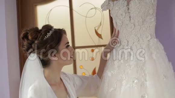 美丽可爱的新娘穿着睡衣站在婚纱附近结婚的早晨漂亮又整洁的女人慢动作视频的预览图