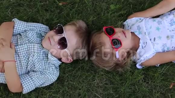 公园里的草地上躺着两个戴太阳镜的小孩子从顶部看视频的预览图