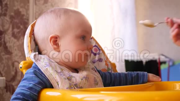 妈妈用勺子在高高的黄色椅子上喂小可爱的男孩视频的预览图