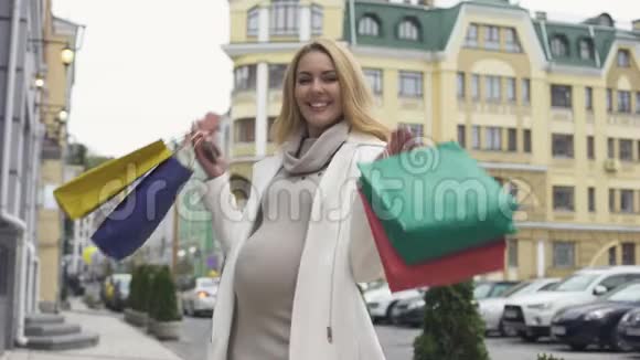 怀着快乐的孕妇手里拿着购物袋和智能手机视频的预览图