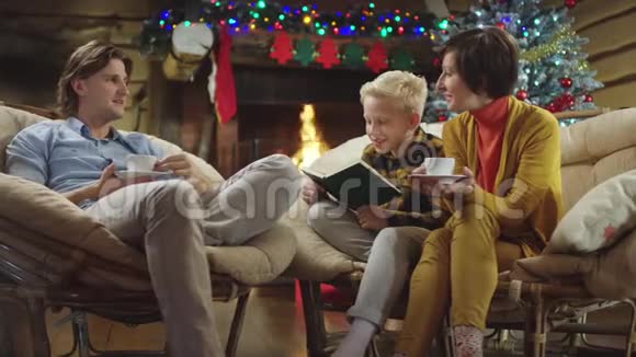 年轻人和女人一边喝咖啡一边聊天小男孩一边读圣诞节的书视频的预览图