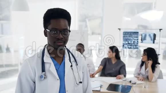 有魅力的非洲男医生看着镜头在医院的背景上有一队考克视频的预览图