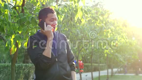 夏天阳光明媚的公园里年轻的亚洲帅哥在打电话视频的预览图