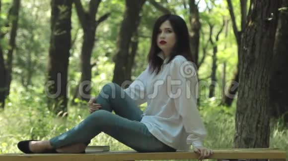 漂亮的黑发女人坐在公园的长凳上视频的预览图