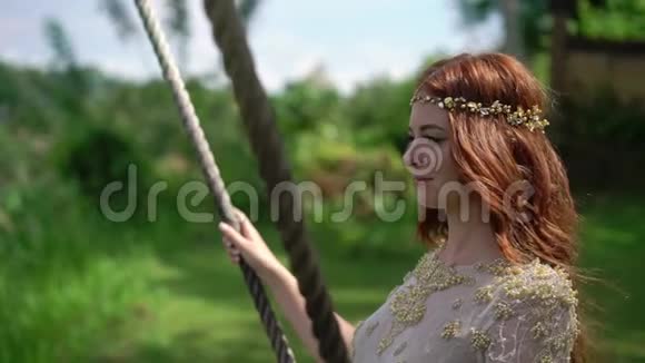 一个年轻的女人在巴厘岛的一个悬崖上荡秋千红发新娘在她的婚礼庆祝日视频的预览图