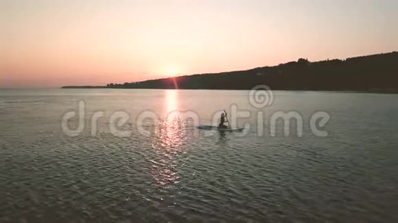 站在桨板上的年轻女人的剪影日落时的鸟瞰视频的预览图
