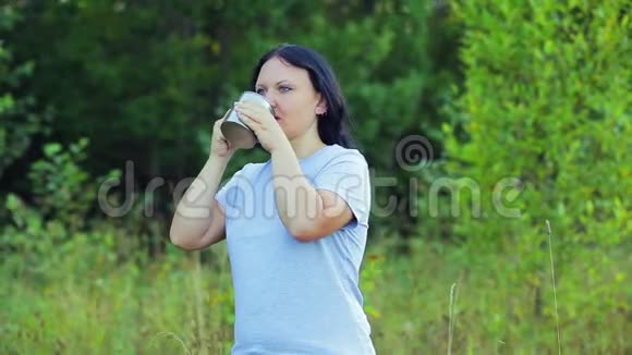 年轻快乐的女人站在森林的边缘喝茶欣赏大自然视频的预览图