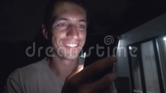 微笑的年轻人晚上在房子前面用智能手机视频的预览图