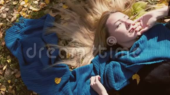 在阳光明媚的日子里秋天的金发美女躺在树叶上慢动作3840x2160视频的预览图