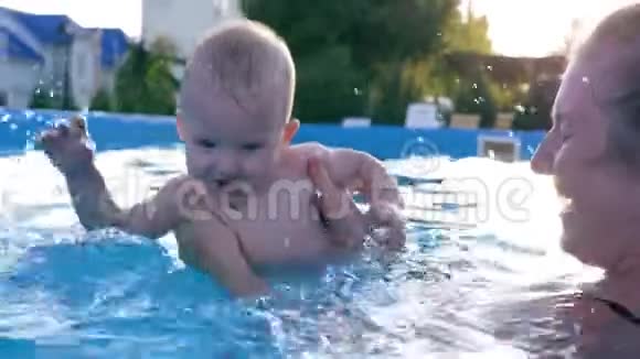 快乐的婴儿在游泳池里溅起水花小男孩和妈妈在夏天的炎热的日子里玩得开心视频的预览图