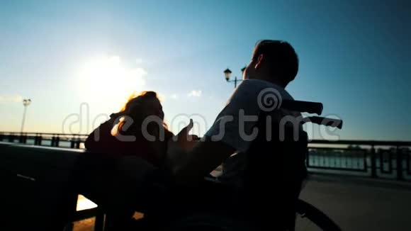 在日落时分坐在轮椅上和女孩聊天的男人视频的预览图