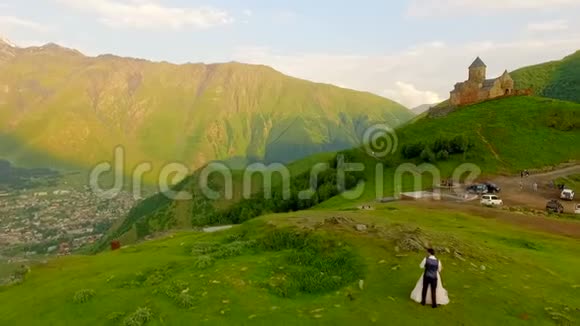 在一座古老城堡的背景下在草地上的新婚夫妇格鲁吉亚卡兹贝吉视频的预览图