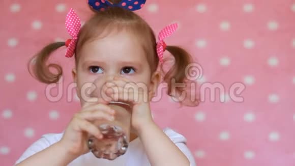 这个小女孩用粉红色背景的玻璃杯子喝水视频的预览图
