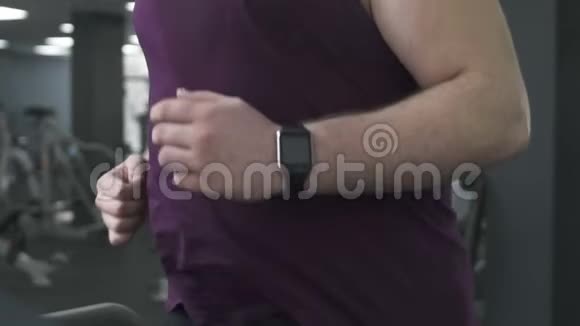 自信的运动员用智能手表在跑步机上跑步控制他的指标视频的预览图