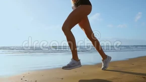 紧身的腿部运动女性穿着白色运动鞋沿着美丽的沙滩奔跑健康的生活方式慢动作视频的预览图