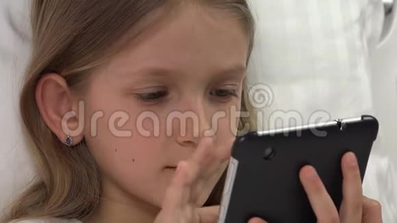 儿童肖像播放平板电脑在床上女孩放松不睡4K视频的预览图