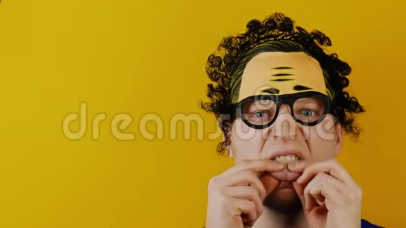 无知的人用手指握住他的舌头卷曲的黑发在黄色的墙上欢快地表达着人类的情感视频的预览图