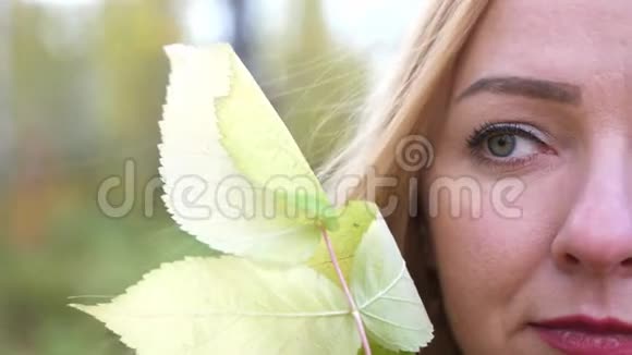 一个美丽的金发女孩的半张脸秋天的树叶在森林里4K慢动作3840x2160视频的预览图