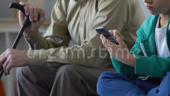 小男孩玩智能手机游戏和爷爷坐在一起感到无聊视频的预览图