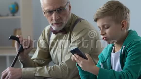 不高兴的爷爷看着孙子滚动智能手机缺乏沟通视频的预览图