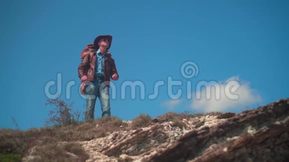 在山上一个男人戴着牛仔帽皮夹克蓝色牛仔裤肩膀上有一个大型旅游背包视频的预览图