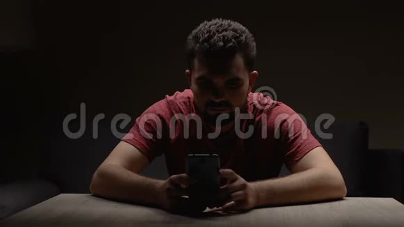 沮丧的男人坐在黑暗的空房间里带着智能手机等待电话视频的预览图
