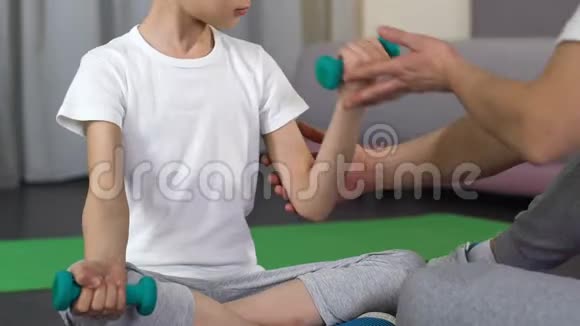 男孩坐着举起哑铃与教练支持父亲帮助健身视频的预览图
