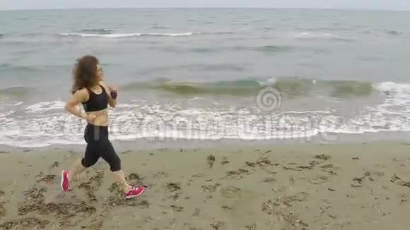 美丽的卷发女子在海滨海滩奔跑积极健康的生活方式视频的预览图