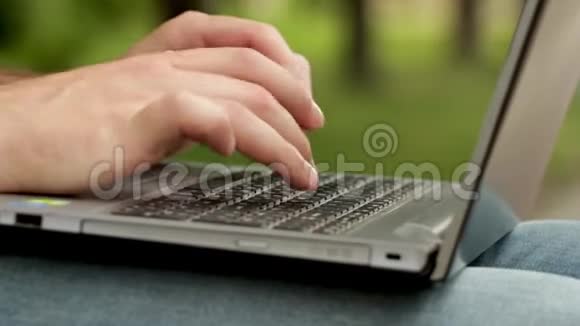 男人手指在笔记本电脑的键盘上打字他用腿拿着电脑男人坐在公园外面他是视频的预览图