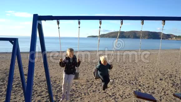 一个三岁的男孩和一个六岁的女孩在一个阳光明媚的早晨在海岸上荡秋千视频的预览图