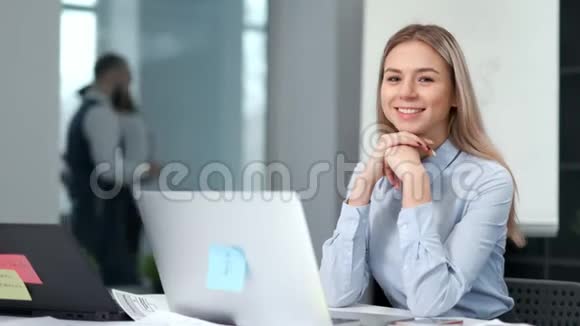 微笑迷人的年轻女商人或办公室职员坐在工作场所的肖像视频的预览图
