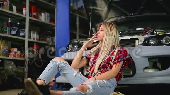 金发可爱的金发女孩坐在车库里的汽车旁累得筋疲力尽每天下班后抽烟视频的预览图