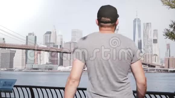 快乐的男性游客来到史诗般的布鲁克林大桥河岸栅栏天际线在纽约市举起双臂张开视频的预览图
