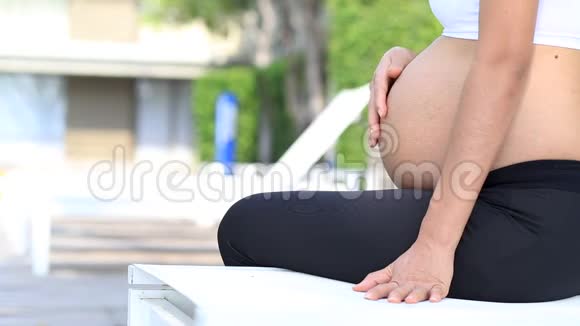 美丽的怀孕少女在公园里放松坐着摸肚子的女孩视频的预览图