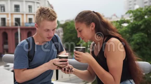 两个年轻人在城市里聊天喝咖啡和使用智能手机视频的预览图