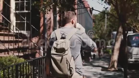 年轻的白人男性游客带着背包沿着阳光明媚的夏季城市街道在纽约喝咖啡视频的预览图