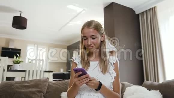 美丽的白种人学生女孩坐在床上使用智能手机微笑着她的小妹妹有趣地跳在她身后视频的预览图