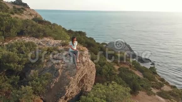 女人坐在岩石上看海景视频的预览图