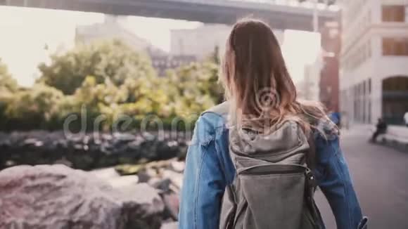 镜头跟随年轻的女游客背着背包沿着阳光明媚的布鲁克林公园河堤慢动作视频的预览图