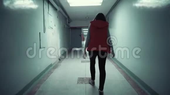 年轻的黑发女子穿着红色无袖上衣走着长长的黑暗走廊视频的预览图