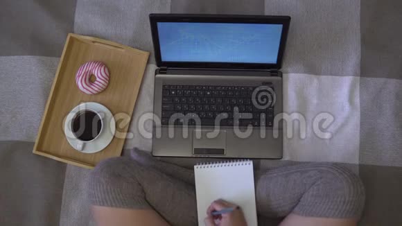 头顶镜头女孩在笔记本电脑旁边的床上画了一张图还有一杯带甜甜圈的咖啡视频的预览图