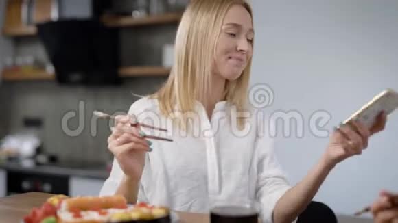 一位年轻的金发女人在家吃寿司的时候接电话她正在按手机视频的预览图