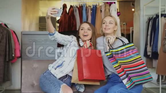 可爱的女孩子在女装精品店里用五颜六色的纸袋自拍然后用智能手机观看视频的预览图
