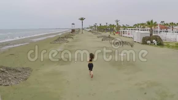 活跃的运动女性在稻草伞之间的海滩上奔跑鸟瞰视频的预览图