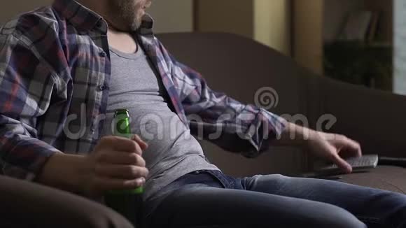 不听话的男人坐在沙发上手里拿着瓶装啤酒看电视休闲视频的预览图