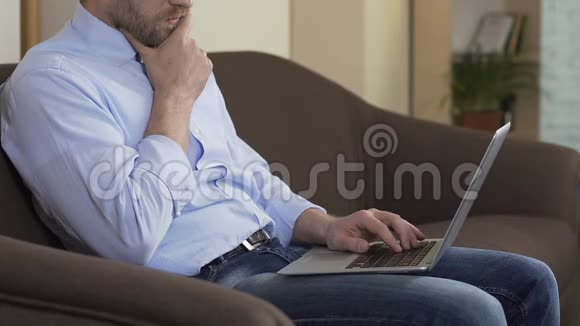 成功的男性自由职业者坐在家里的沙发上在笔记本电脑上工作上网视频的预览图